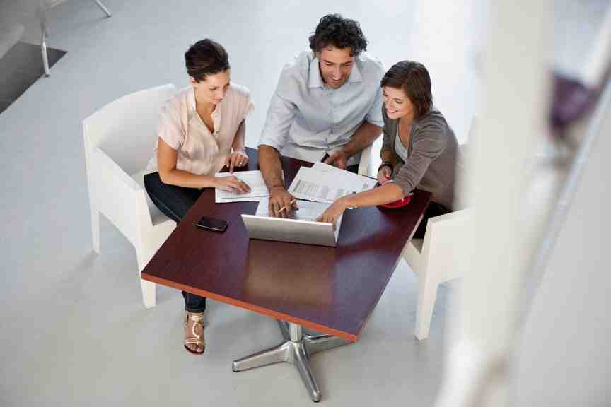 three people sitting at a table working on laptops