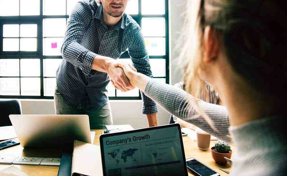 two people shaking hands in front of a laptop