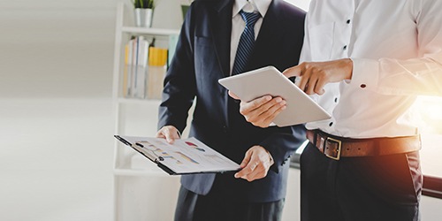 two men in business attire looking at something on a tablet