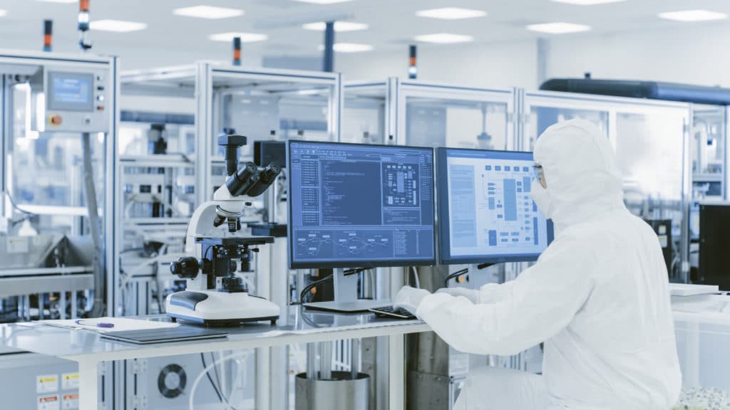 a man in a white lab coat looking at two monitors