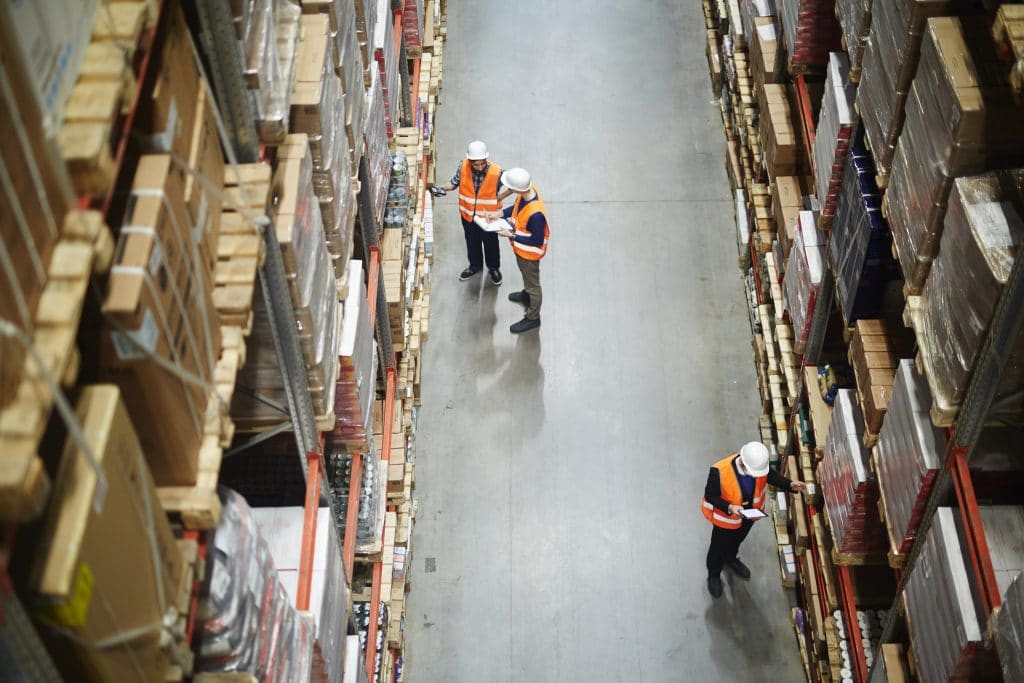 two workers in orange vests and hard hats are walking through a warehouse