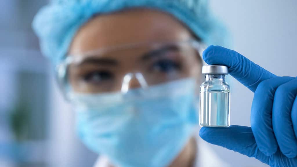 a woman in a medical gown holding up a vial