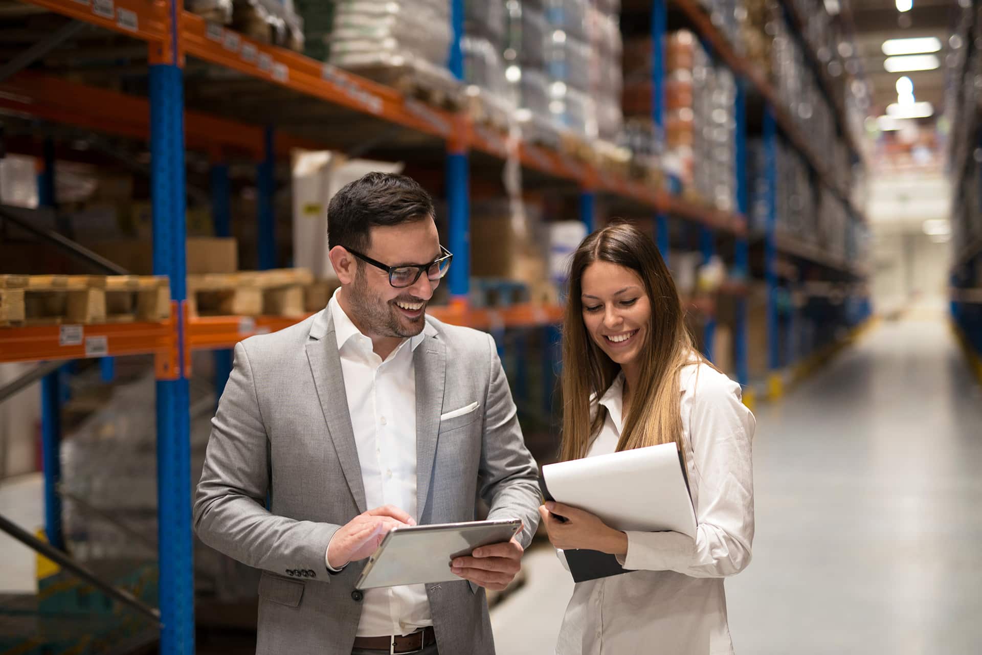 two people standing in a warehouse looking at something on a tablet