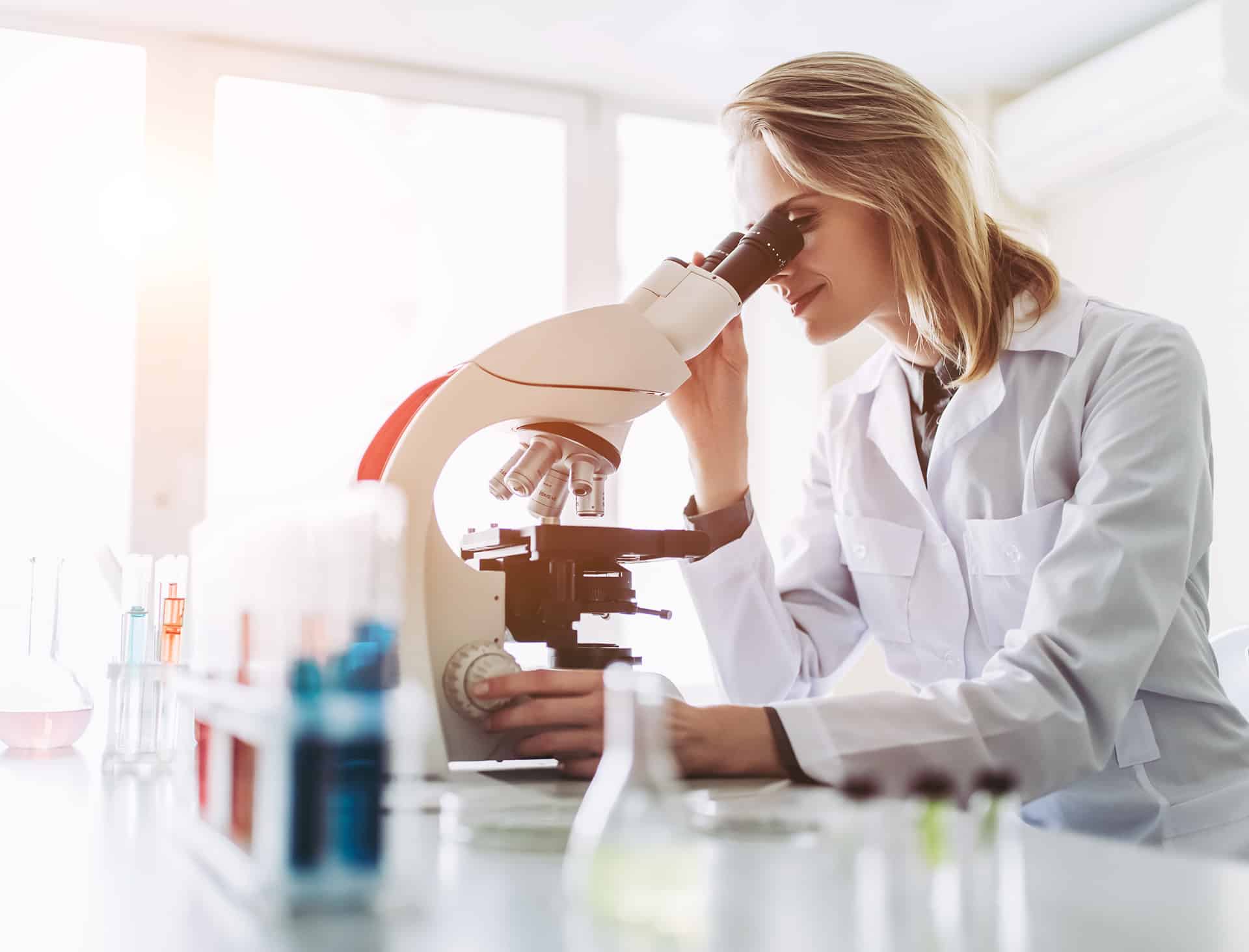 a woman in white lab coat looking through a microscope