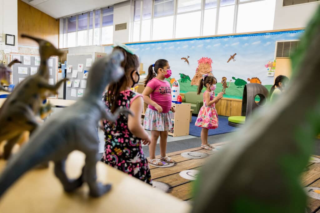 two girls and one boy are looking at dinosaur statues