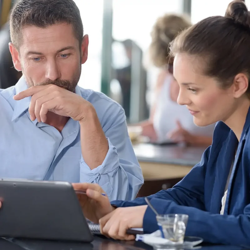 a man and woman sitting at a table looking at a tablet